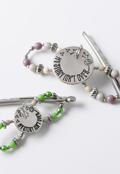 Flexi hair clip with a medallion centerpiece engraved with the phrase "My Story Isn't Over" and a hook to attach charms.