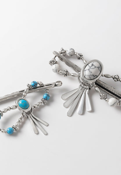 Tabitha Flexi Clip features an oval stoneset with paddle drops and natural howlite stone accents. Available in turquoise and white.