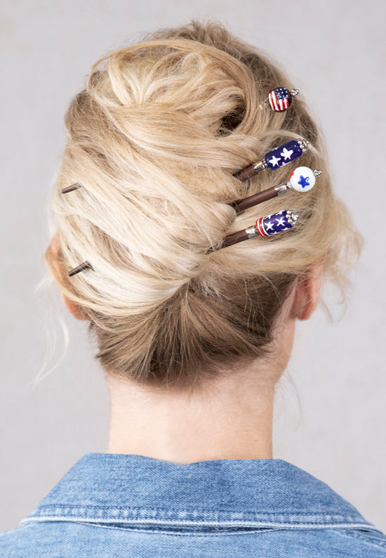Patriotic hair sticks shown in hair in a variety of five designs including stars and stripes of red, white and blue.