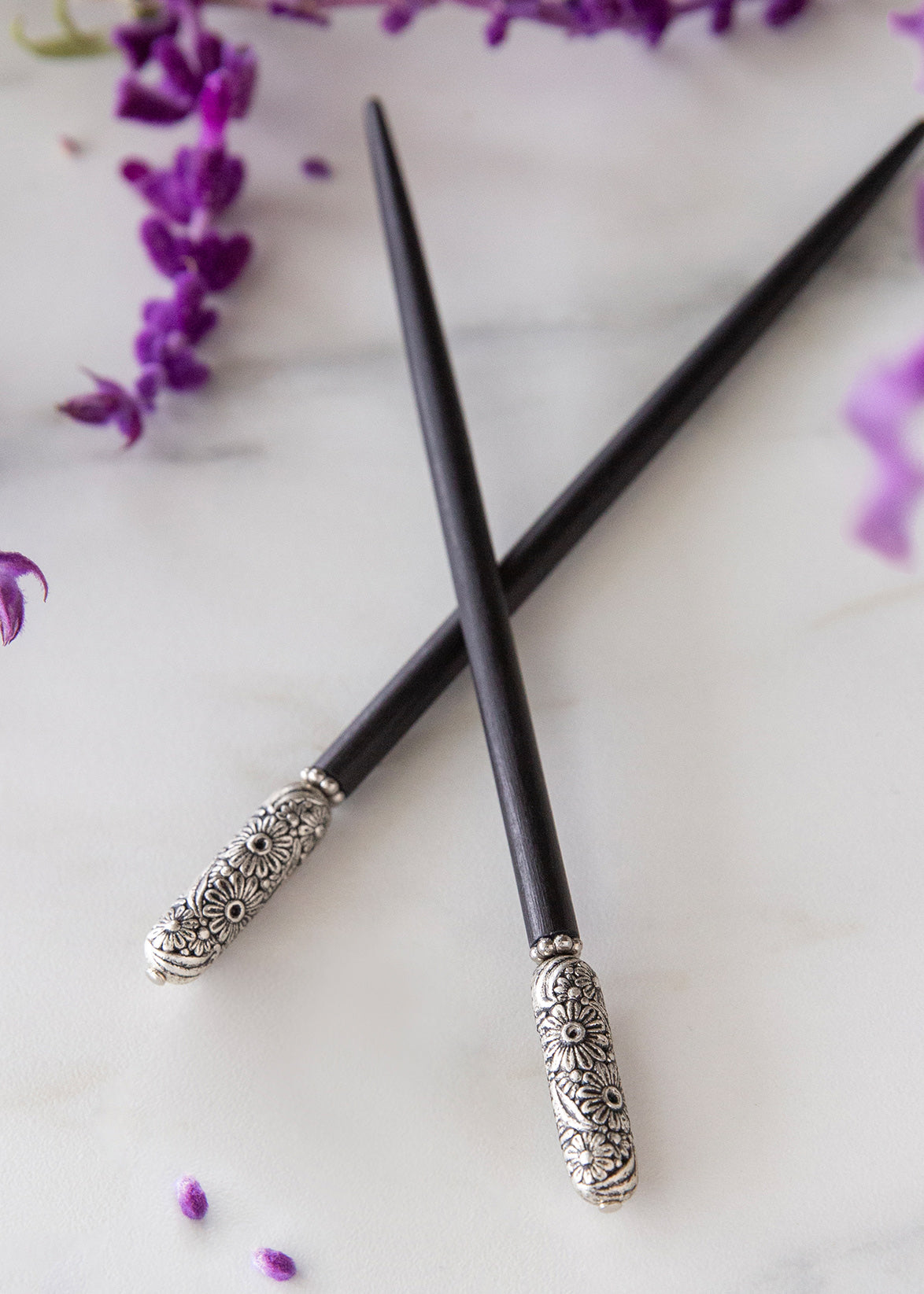 Black chopsticks with silver decorative ends on a white surface with purple flowers.